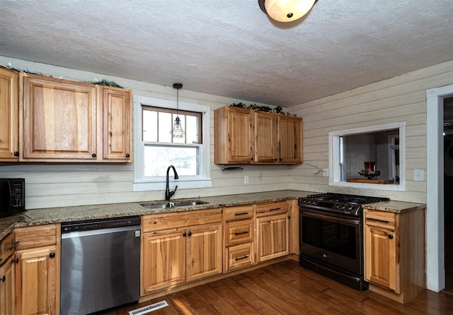 kitchen with sink, black appliances, dark hardwood / wood-style floors, hanging light fixtures, and wood walls