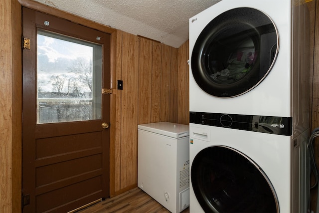 laundry room featuring wood walls, dark hardwood / wood-style flooring, a textured ceiling, and stacked washer and clothes dryer