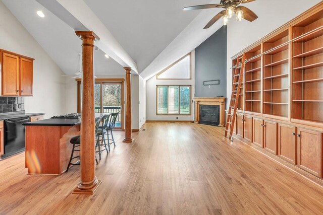 kitchen featuring ornate columns, ceiling fan, dishwasher, vaulted ceiling, and a kitchen bar