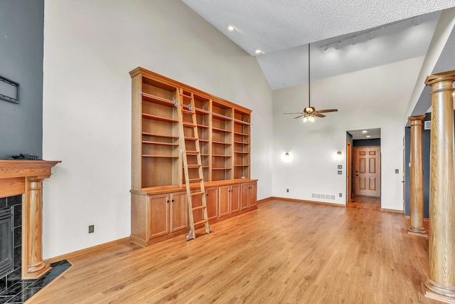 unfurnished living room featuring light wood-type flooring, a textured ceiling, ceiling fan, a tile fireplace, and high vaulted ceiling