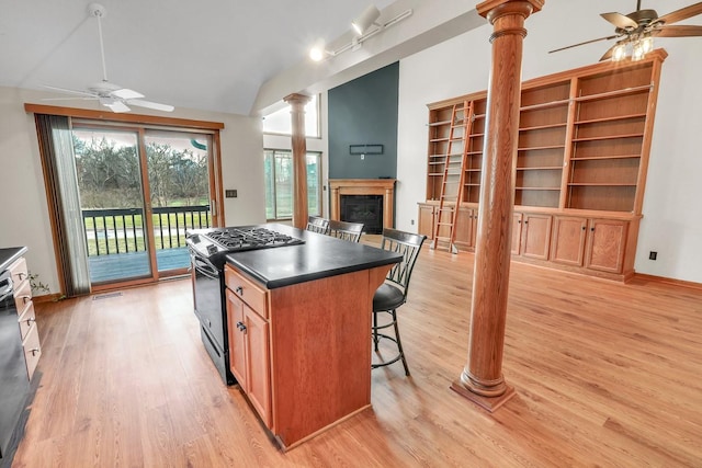 kitchen with a kitchen bar, decorative columns, black gas range oven, vaulted ceiling, and a kitchen island