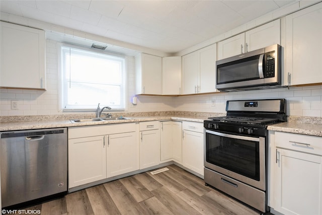 kitchen with decorative backsplash, appliances with stainless steel finishes, sink, light hardwood / wood-style flooring, and white cabinetry