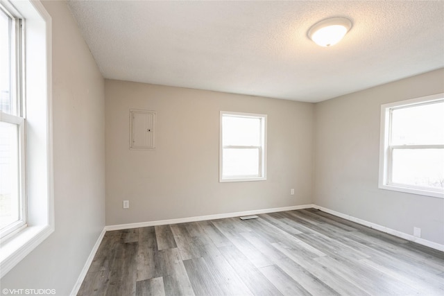 empty room with a textured ceiling, light hardwood / wood-style floors, and electric panel