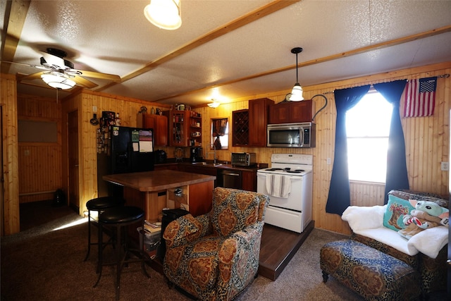 kitchen featuring dark colored carpet, a textured ceiling, stainless steel appliances, and wood walls