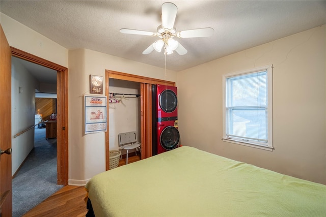 bedroom featuring stacked washer and dryer, ceiling fan, a textured ceiling, wood-type flooring, and a closet