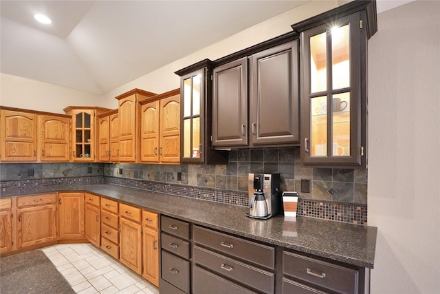 kitchen featuring dark stone countertops, decorative backsplash, light tile patterned floors, and lofted ceiling