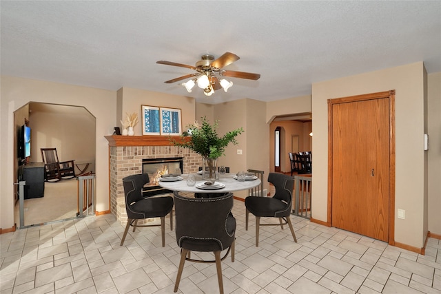 dining room with ceiling fan, a fireplace, and a textured ceiling