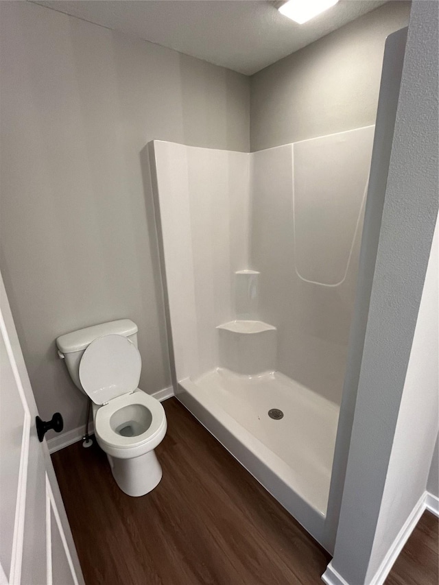 bathroom with hardwood / wood-style flooring, a shower, and toilet