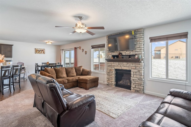 living room featuring carpet flooring, a stone fireplace, ceiling fan, and a textured ceiling