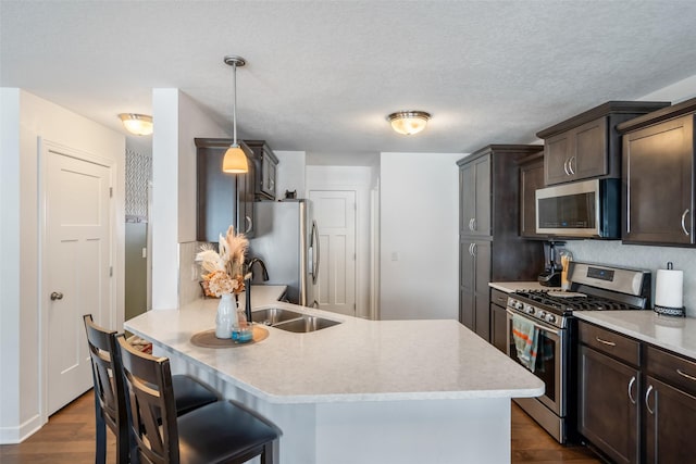 kitchen featuring sink, dark wood-type flooring, hanging light fixtures, dark brown cabinets, and appliances with stainless steel finishes