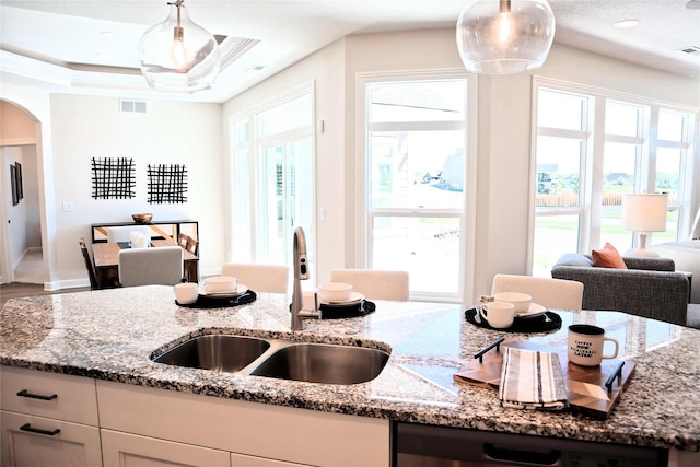 kitchen with light stone counters, sink, pendant lighting, and stainless steel dishwasher