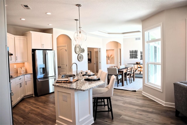 kitchen with stainless steel fridge with ice dispenser, white cabinetry, plenty of natural light, and a kitchen island with sink