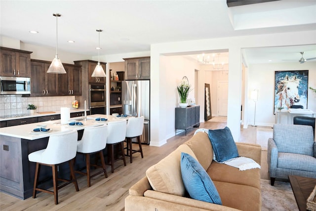 kitchen with a kitchen island with sink, appliances with stainless steel finishes, decorative light fixtures, light hardwood / wood-style floors, and a breakfast bar area