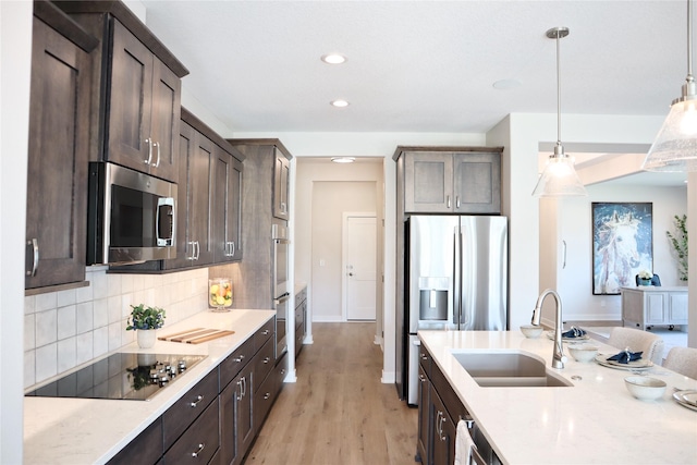 kitchen with appliances with stainless steel finishes, light wood-type flooring, dark brown cabinets, sink, and decorative light fixtures