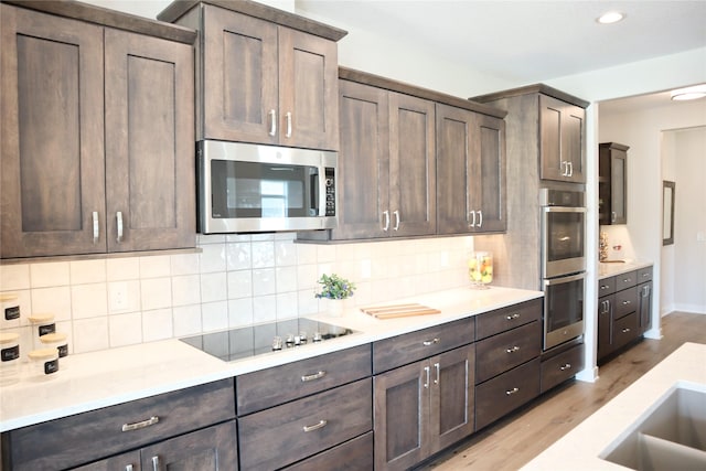 kitchen with light stone countertops, stainless steel appliances, tasteful backsplash, light hardwood / wood-style floors, and dark brown cabinets