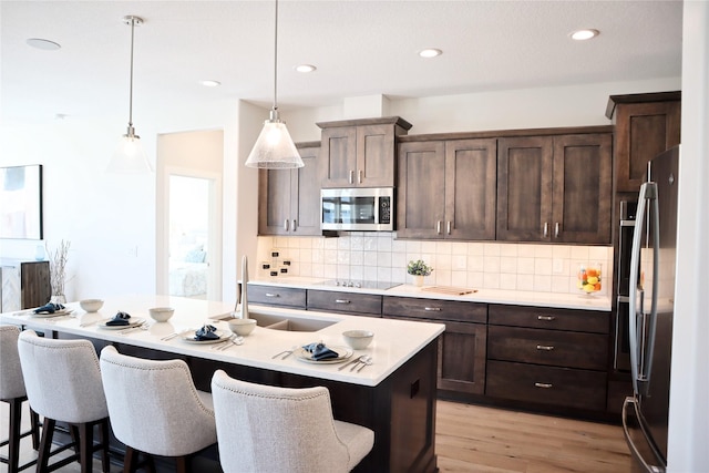 kitchen with a breakfast bar, stainless steel appliances, a kitchen island with sink, sink, and pendant lighting