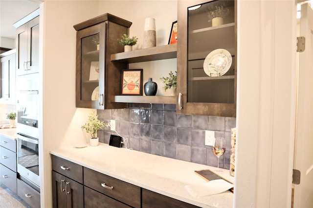 kitchen featuring decorative backsplash, dark brown cabinetry, oven, and light stone countertops