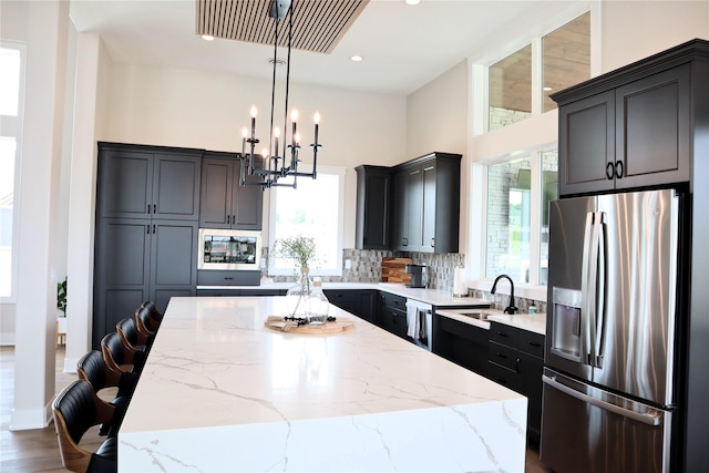 kitchen featuring a kitchen bar, light stone counters, stainless steel appliances, a center island, and hanging light fixtures