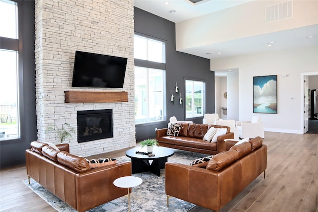 living room featuring light hardwood / wood-style floors, a towering ceiling, and a fireplace