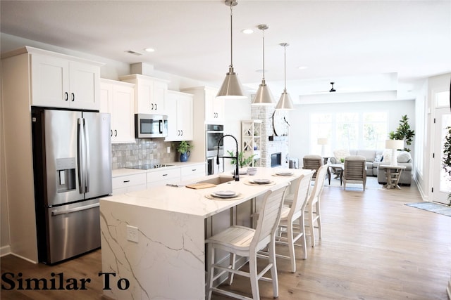 kitchen featuring a kitchen island with sink, white cabinets, pendant lighting, and appliances with stainless steel finishes