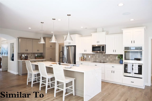 kitchen featuring white cabinetry, backsplash, pendant lighting, a kitchen island with sink, and appliances with stainless steel finishes