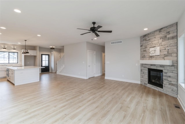 unfurnished living room with ceiling fan, a fireplace, and light wood-type flooring