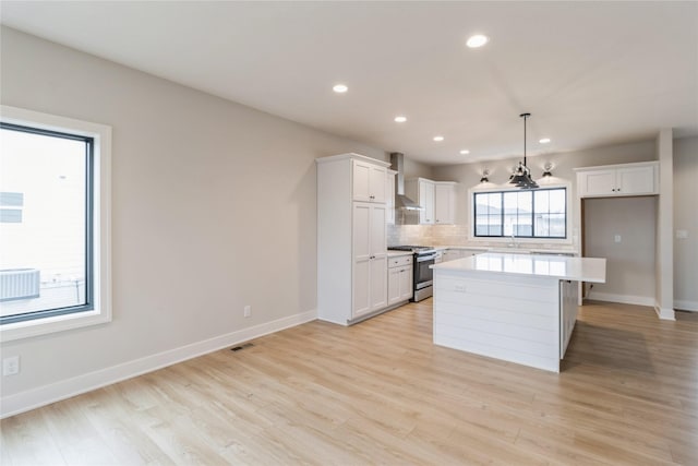 kitchen featuring stainless steel gas stove, a center island, wall chimney range hood, pendant lighting, and white cabinets