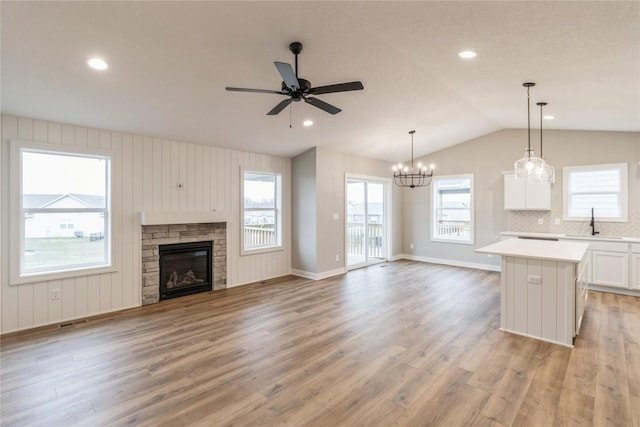 kitchen featuring a stone fireplace, a kitchen island, pendant lighting, white cabinetry, and lofted ceiling