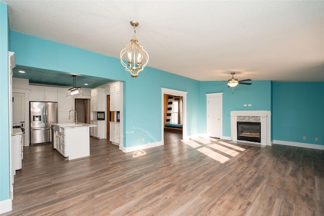 unfurnished living room featuring sink, dark wood-type flooring, a high end fireplace, a textured ceiling, and ceiling fan with notable chandelier