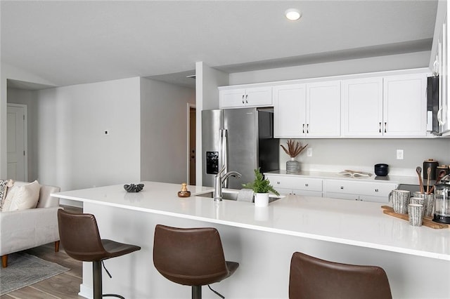 kitchen featuring a kitchen bar, stainless steel refrigerator with ice dispenser, sink, wood-type flooring, and white cabinetry