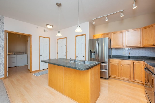 kitchen with stainless steel appliances, decorative light fixtures, a kitchen island with sink, washer and dryer, and light wood-type flooring