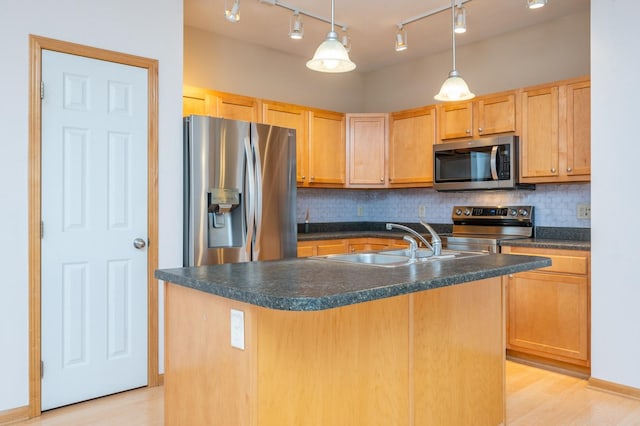 kitchen with sink, stainless steel appliances, light hardwood / wood-style floors, decorative light fixtures, and a center island with sink