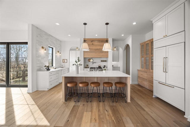 kitchen featuring white cabinetry, a kitchen breakfast bar, paneled fridge, a center island with sink, and light hardwood / wood-style flooring