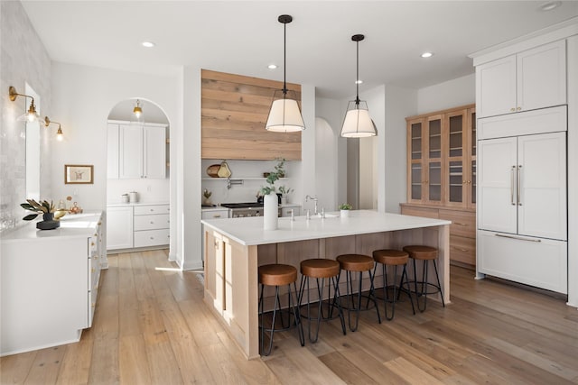 kitchen featuring paneled refrigerator, a center island with sink, and white cabinets