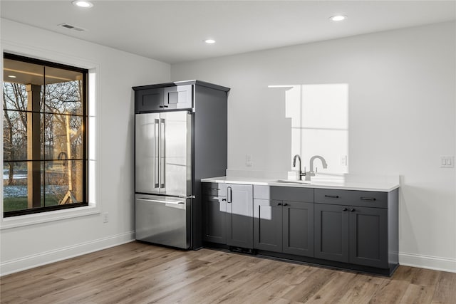 kitchen featuring high end fridge, sink, gray cabinets, and light wood-type flooring