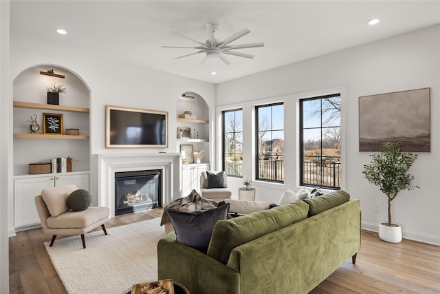 living room featuring built in shelves, light hardwood / wood-style flooring, and ceiling fan