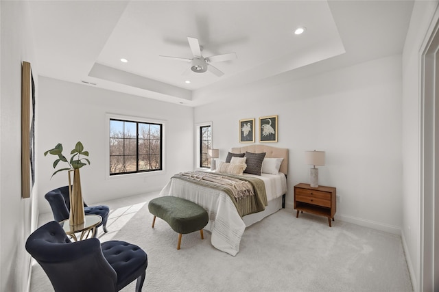 bedroom featuring a raised ceiling, light colored carpet, and ceiling fan