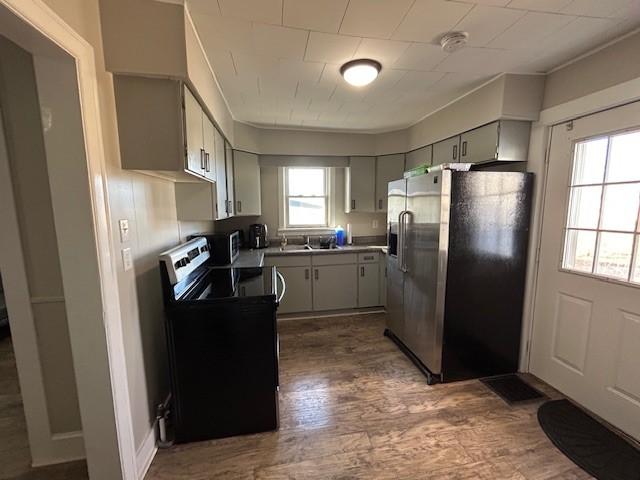 kitchen with stainless steel fridge, black range with electric cooktop, hardwood / wood-style flooring, and gray cabinetry