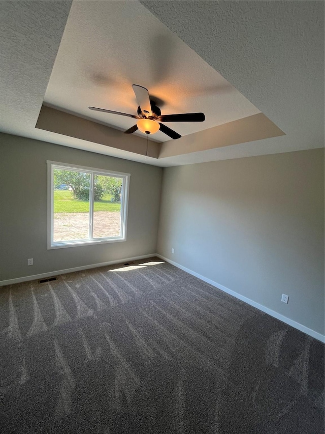 empty room with ceiling fan, carpet flooring, a raised ceiling, and a textured ceiling