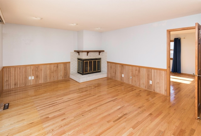 unfurnished living room featuring a brick fireplace, light hardwood / wood-style flooring, and wood walls