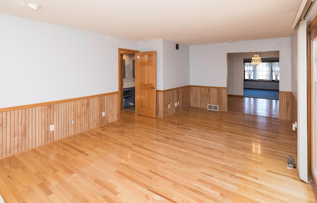 spare room featuring a chandelier, wood walls, and light hardwood / wood-style flooring