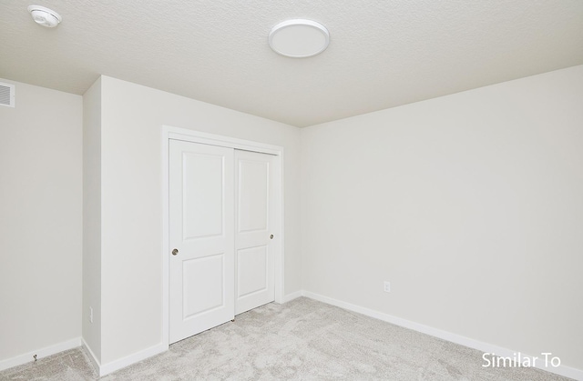 unfurnished bedroom featuring light colored carpet, a closet, and a textured ceiling