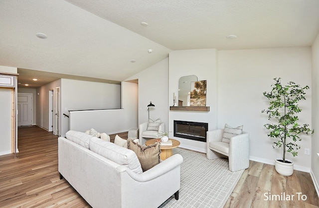 living room featuring lofted ceiling, light hardwood / wood-style flooring, and a textured ceiling