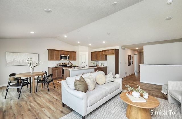 living room with light hardwood / wood-style flooring, sink, vaulted ceiling, and a textured ceiling