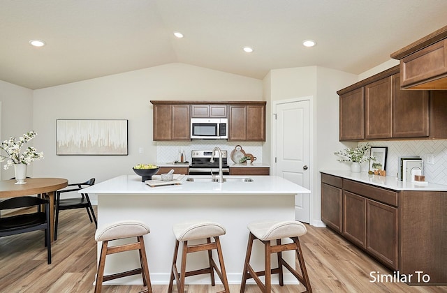 kitchen with sink, vaulted ceiling, a center island with sink, light hardwood / wood-style flooring, and appliances with stainless steel finishes