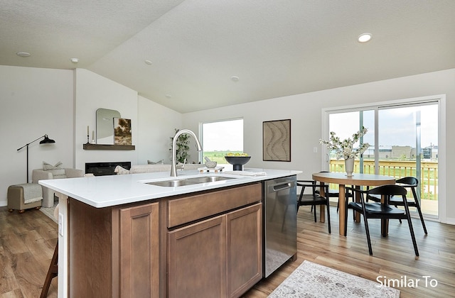 kitchen featuring sink, vaulted ceiling, light wood-type flooring, stainless steel dishwasher, and an island with sink