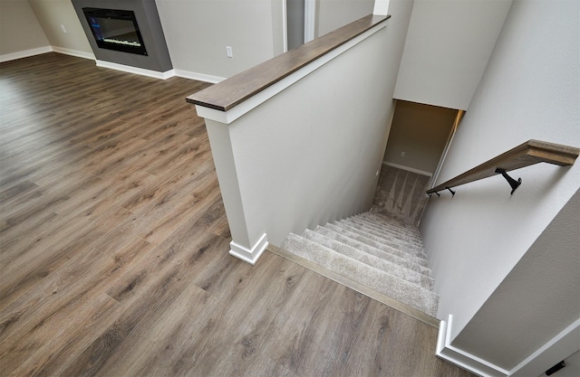 staircase with baseboards, a glass covered fireplace, and wood finished floors