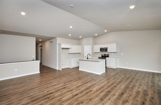 kitchen with white cabinets, appliances with stainless steel finishes, an island with sink, open floor plan, and vaulted ceiling
