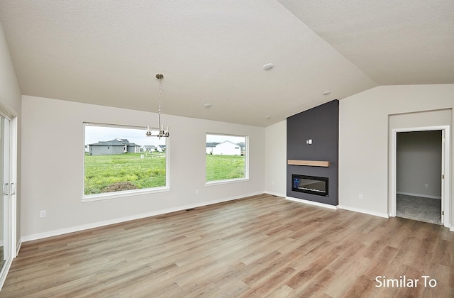 unfurnished living room with vaulted ceiling, a fireplace, light hardwood / wood-style floors, a textured ceiling, and an inviting chandelier