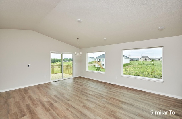 empty room featuring lofted ceiling, a textured ceiling, light hardwood / wood-style floors, and a chandelier